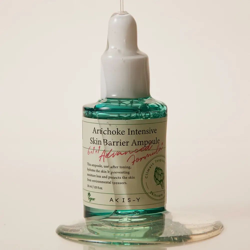 Groene glazen fles met witte dop. Product ligt op een oppervlak. Vloeistof ernaast.