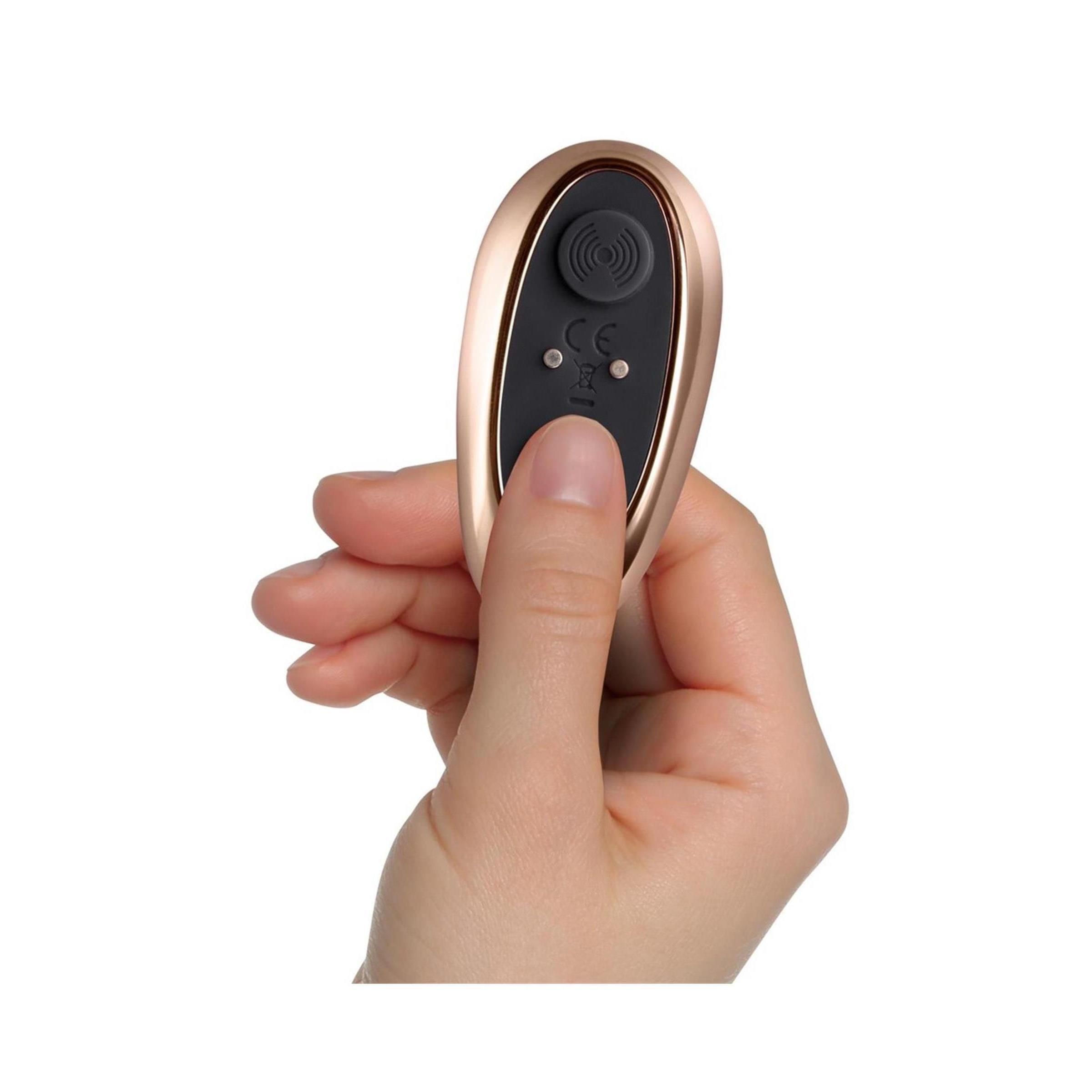 Une main tient une télécommande or rose avec des boutons noirs.