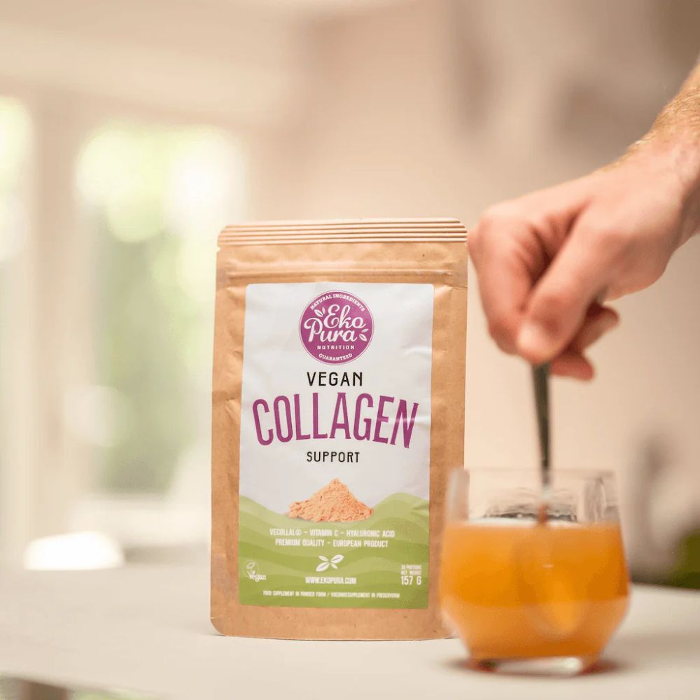 Zak met opschrift Vegan Collagen Support. Lepel roert in glas. Hand houdt lepel vast. Achtergrond: keuken.