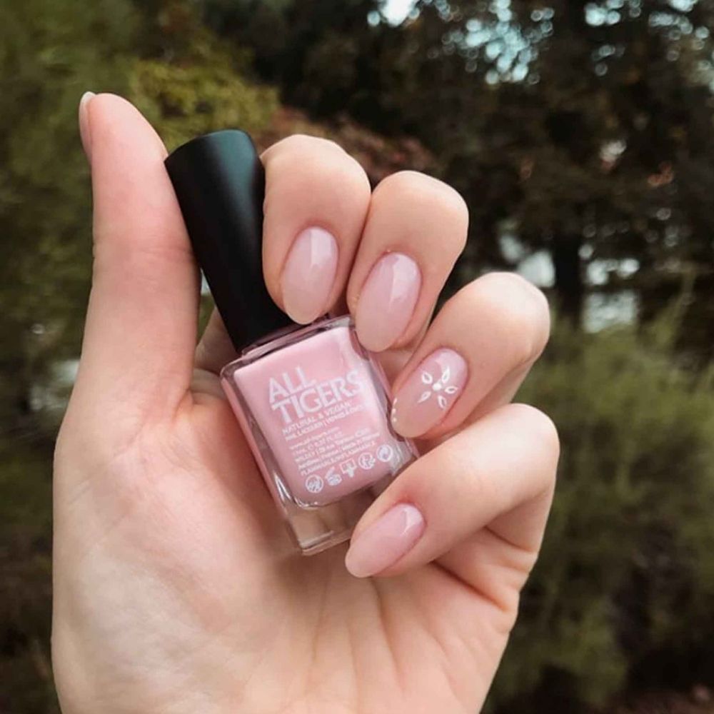 Hand houdt nagellakfles vast. "ALL TIGERS" staat op de fles. Nagels gelakt met roze lak.