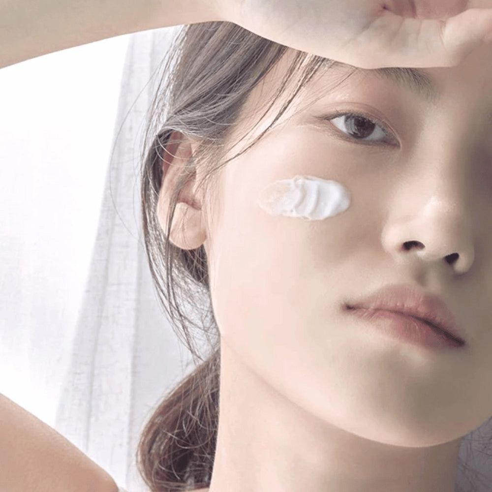 Visage d'une femme avec de la crème sur la joue. Environnement clair.