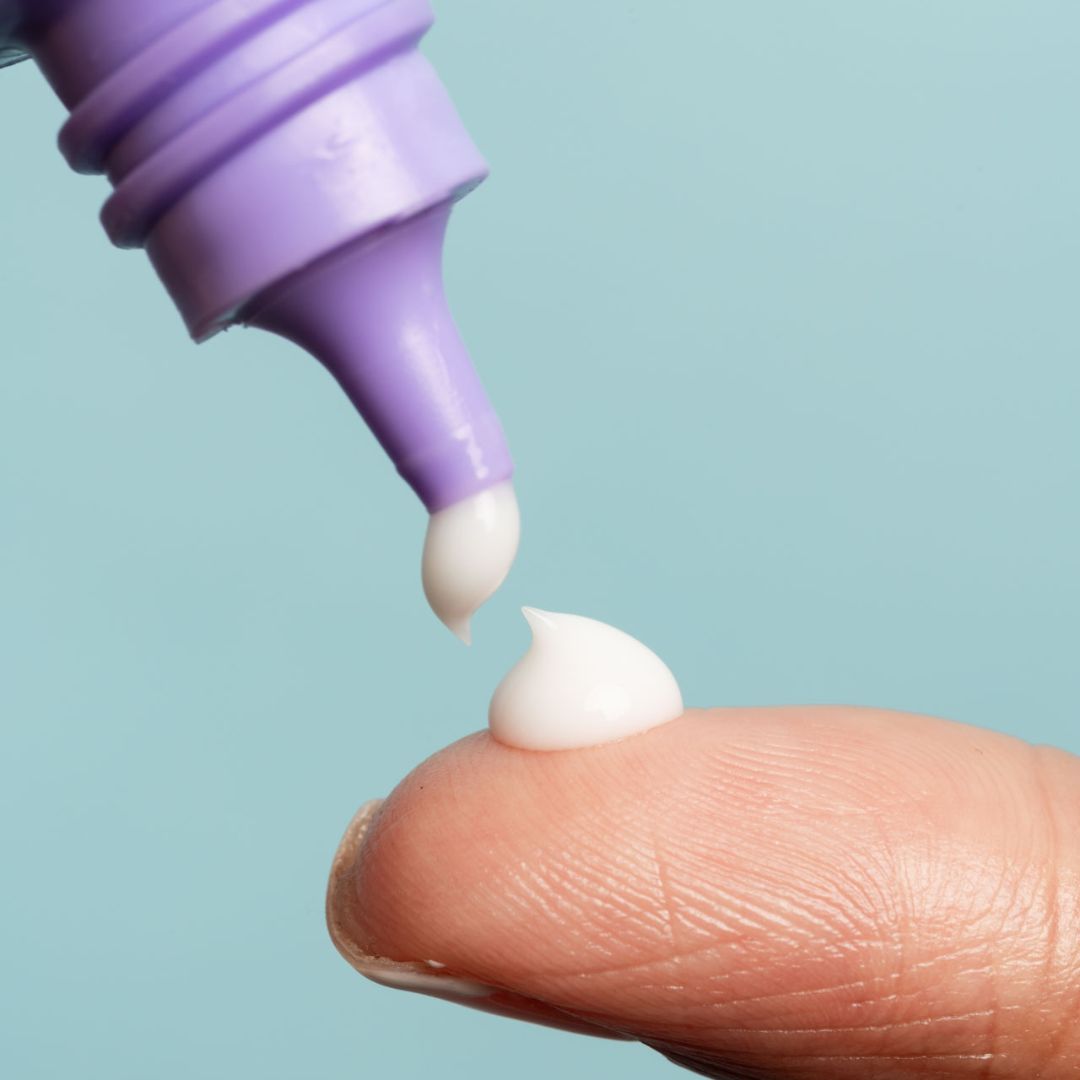 Crème wordt uit een paarse tube op een vinger gedrukt. De crème-druppel is wit.