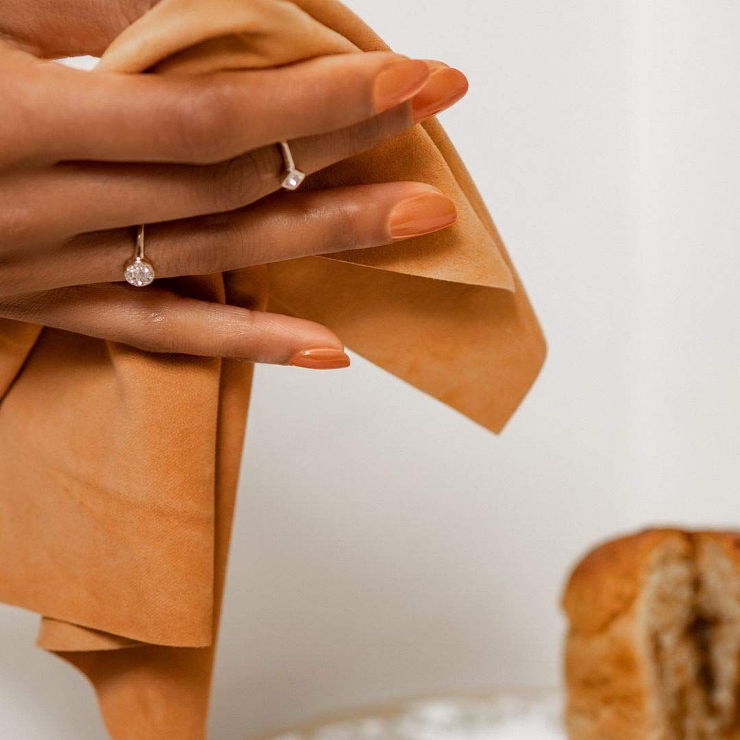 Hand met gelakte, oranje nagels. Houdt een doek vast. Achtergrond: brood.