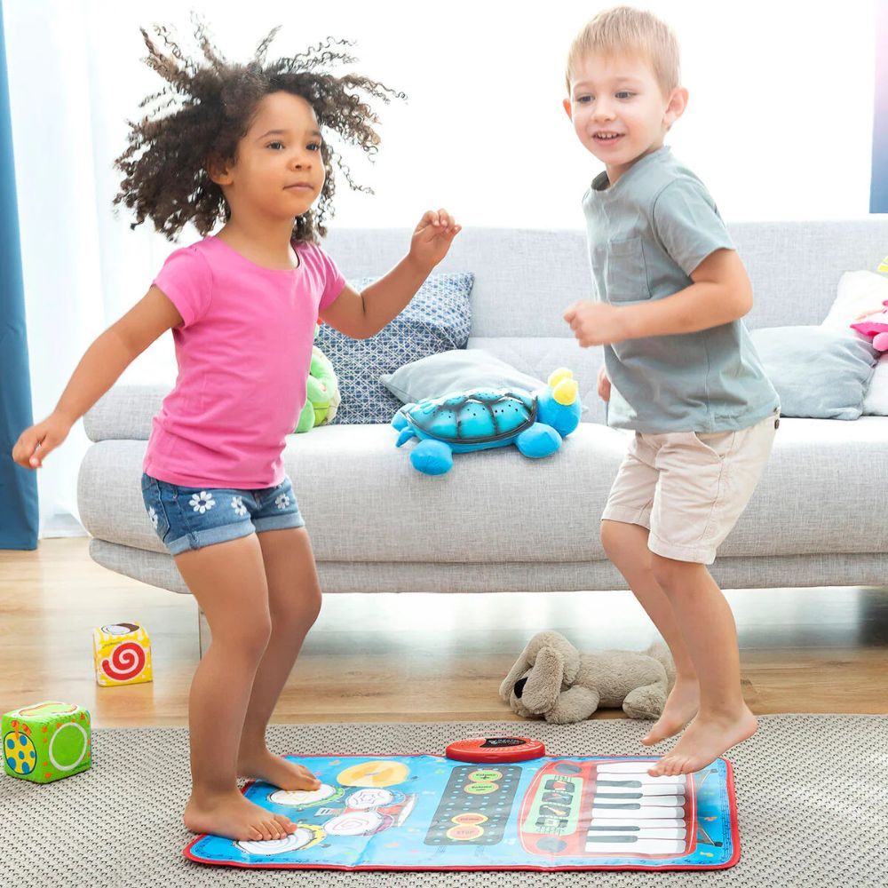 Deux enfants dansent sur un tapis musical bleu. Le tapis a des tambours et des touches de piano. Un canapé et des jouets sont en arrière-plan.