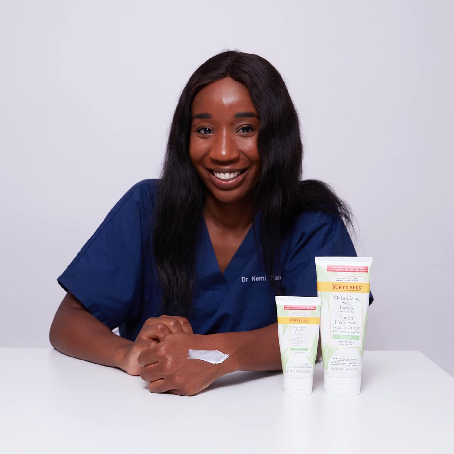 Femme assise à une table avec trois tubes. Un avec "Burt's Bees". De la crème est appliquée sur le bras.