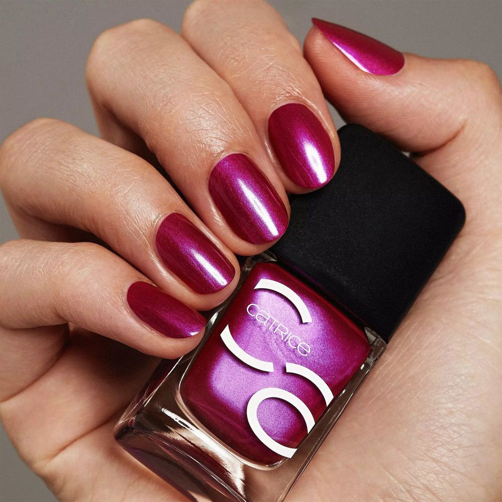 Main avec ongles vernis et flacon de vernis à ongles. Ongles violets, flacon avec bouchon noir, marque Catrice.