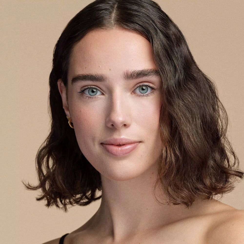 Portrait d'une femme aux yeux bleus et aux cheveux bruns ondulés. Elle ne porte pas de maquillage.