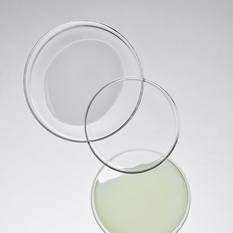 Drie transparante schalen met vloeistof. Een schaal met groene vloeistof, twee lege schalen.