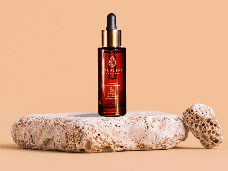 Bruine serumfles met gouden dop. Geplaatst op een steen. Opschrift: Lagalene Milano.