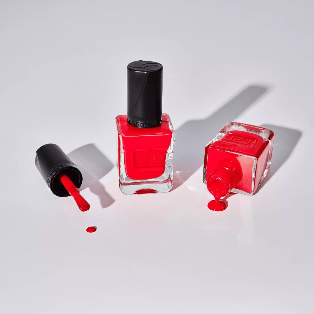 Flacons et gouttes de vernis à ongles. Un flacon avec pinceau, deux flacons avec vernis rouge.