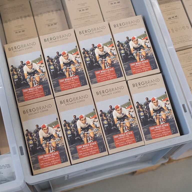 Meerdere koffieverpakkingen BERGBRAND Eddy would Attack in een bak. Opdruk: Eddy would Attack, Specialty Coffee.