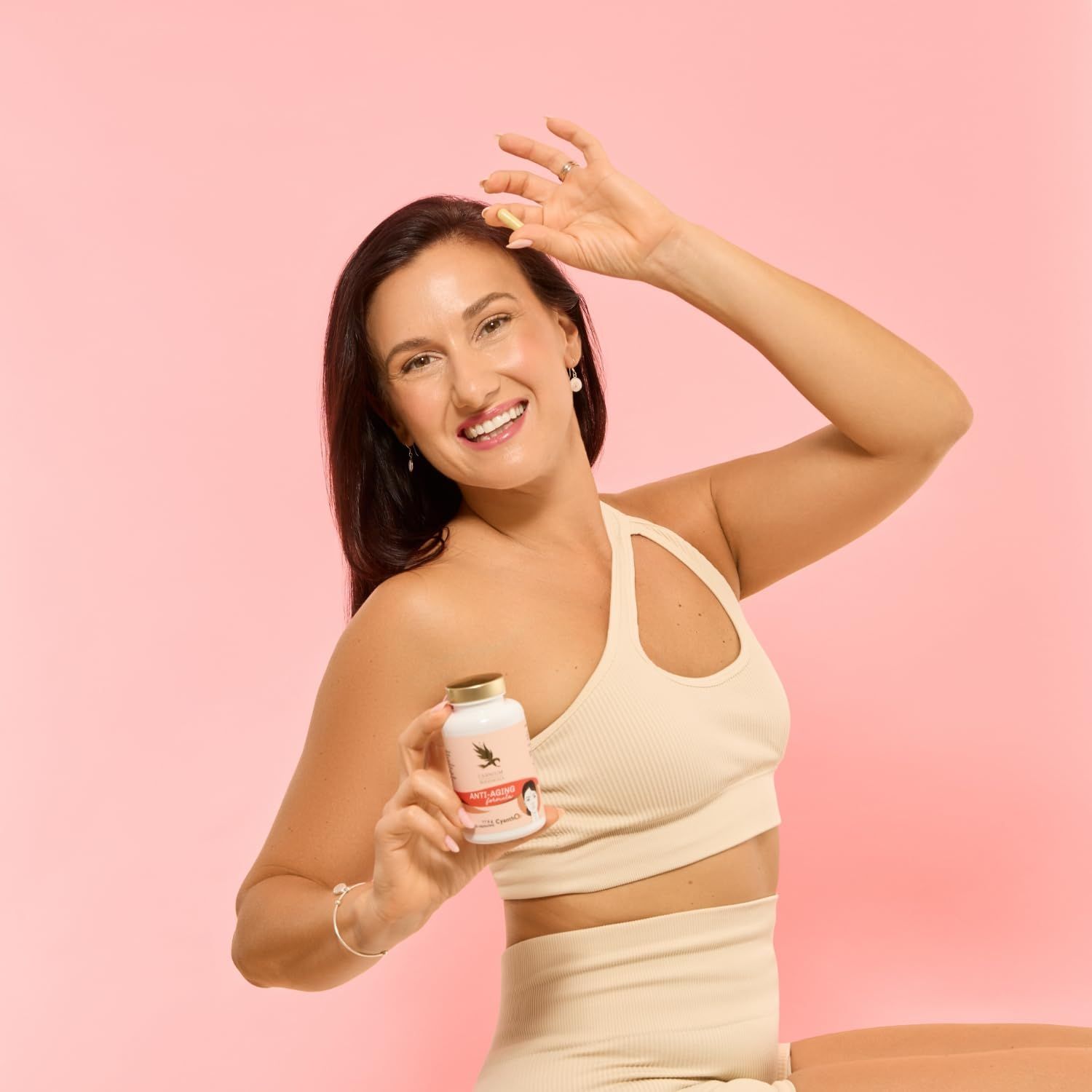 Vrouw houdt pilfles met gouden dop vast. Opschrift: Anti-Aging formula. Vrouw lacht.