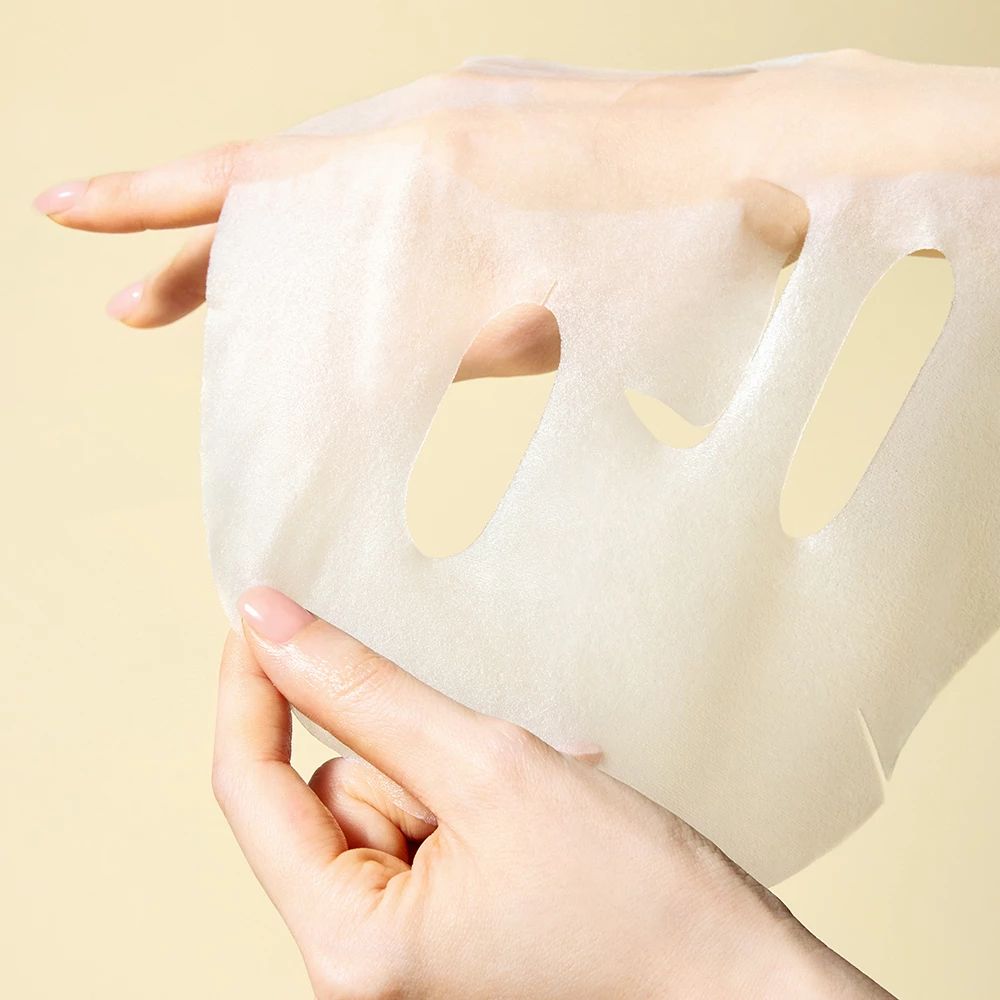 Handen die een wit gezichtsmasker vasthouden met openingen voor ogen en mond.