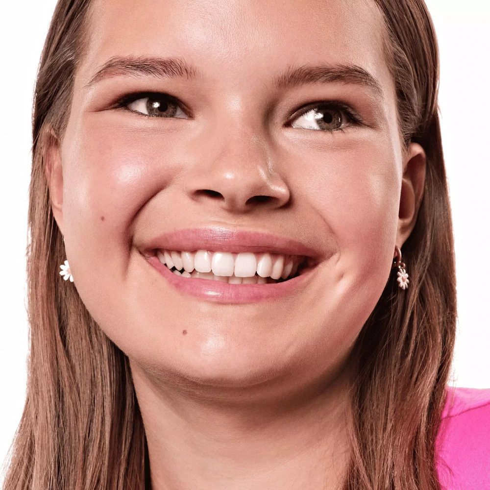 Portrait d'une femme souriante aux cheveux châtain clair. Elle porte des boucles d'oreilles et un haut rose.