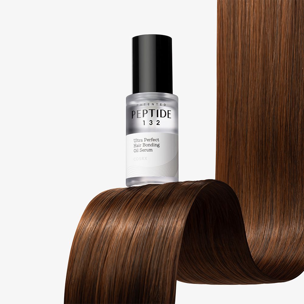Sérum huileux COSRX Peptide 132 Ultra Perfect Hair Bonding dans un flacon en verre sur des cheveux ondulés.