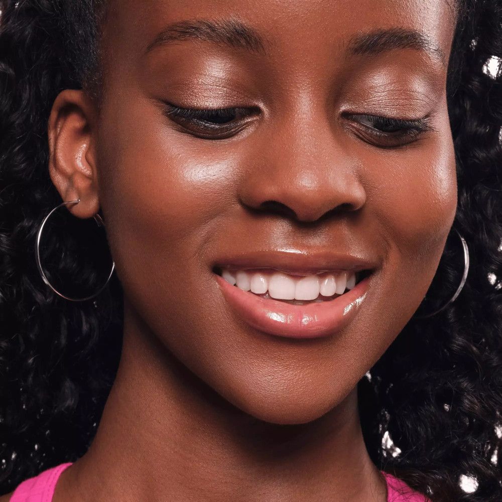 Une femme avec de l'ombre à paupières rose et des boucles d'oreilles. Elle sourit.
