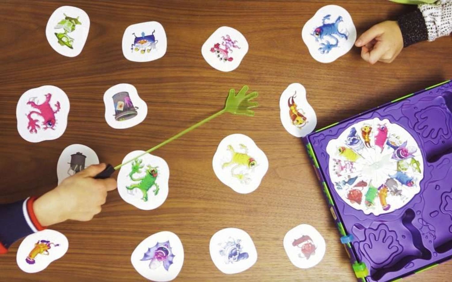 Speelkaarten en spelbord. Een kind grijpt een kaart met een grijpgereedschap. Kaarten met monsterillustraties.