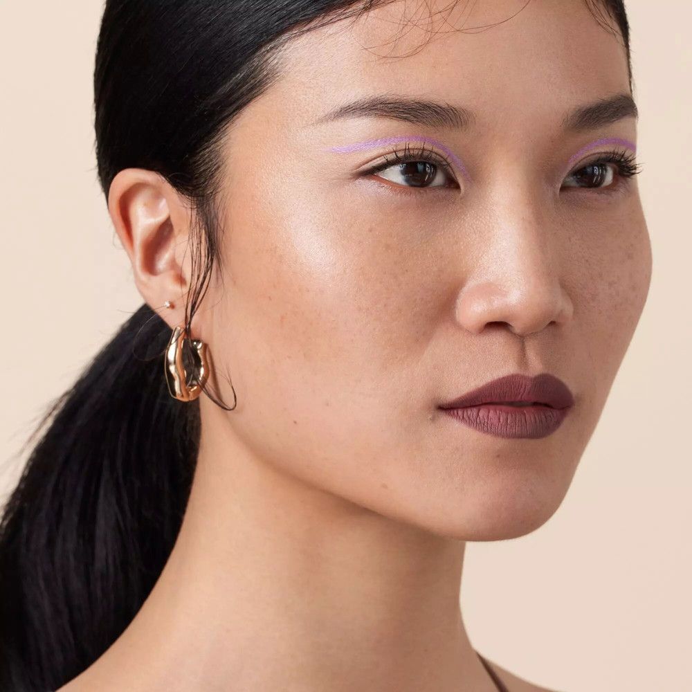 Close-up van een vrouw met een donkere huid. Ze draagt gouden oorbellen en lippenstift.