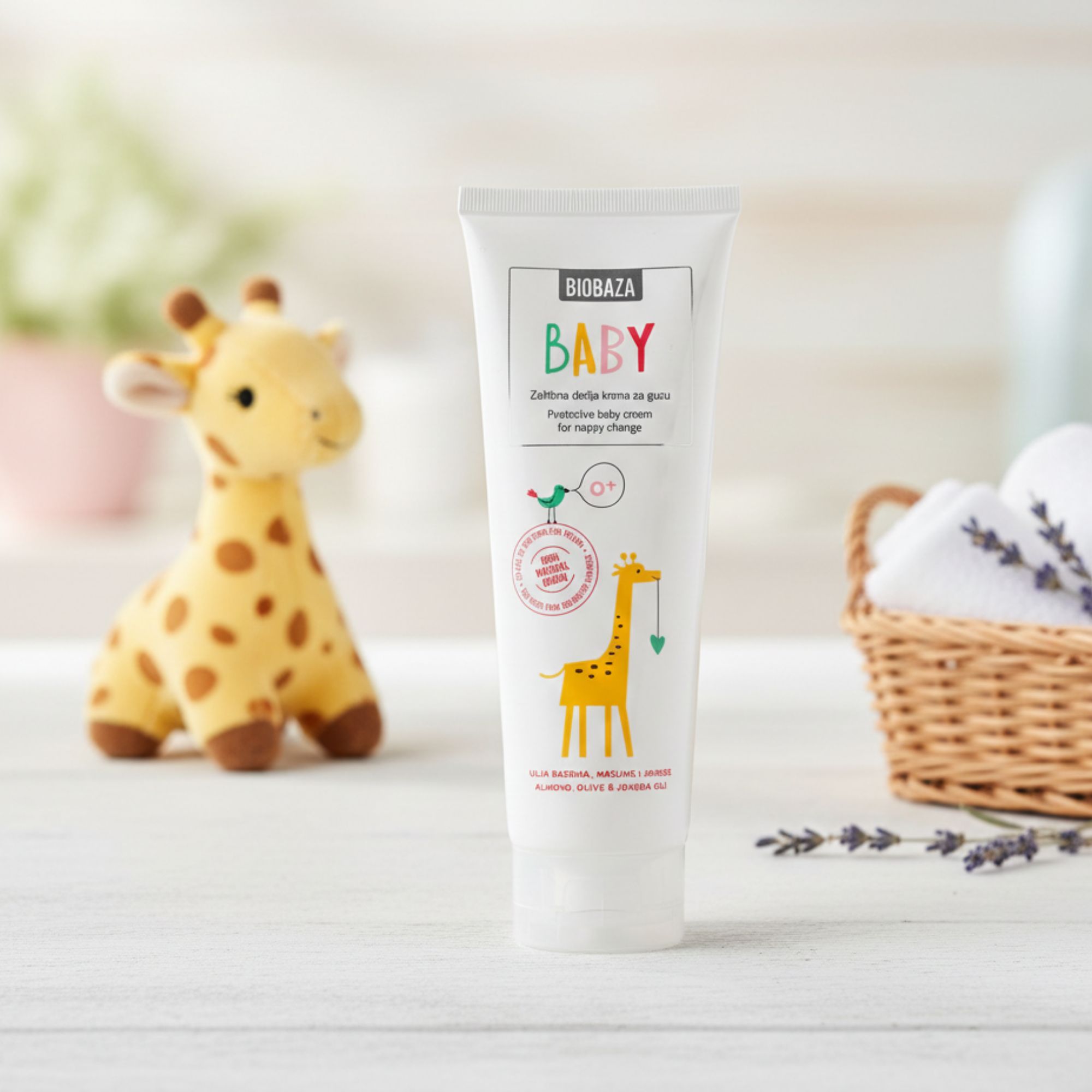 Witte tube met opschrift BABY en giraf-illustratie. Staat naast een knuffel en een mand met handdoeken.