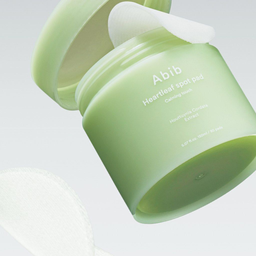 Groene pot, deksel open, pad zichtbaar. Opschrift: Abib Heartleaf spot pad. Tekst eronder: Calming touch, Houttuynia Cordata Extract.