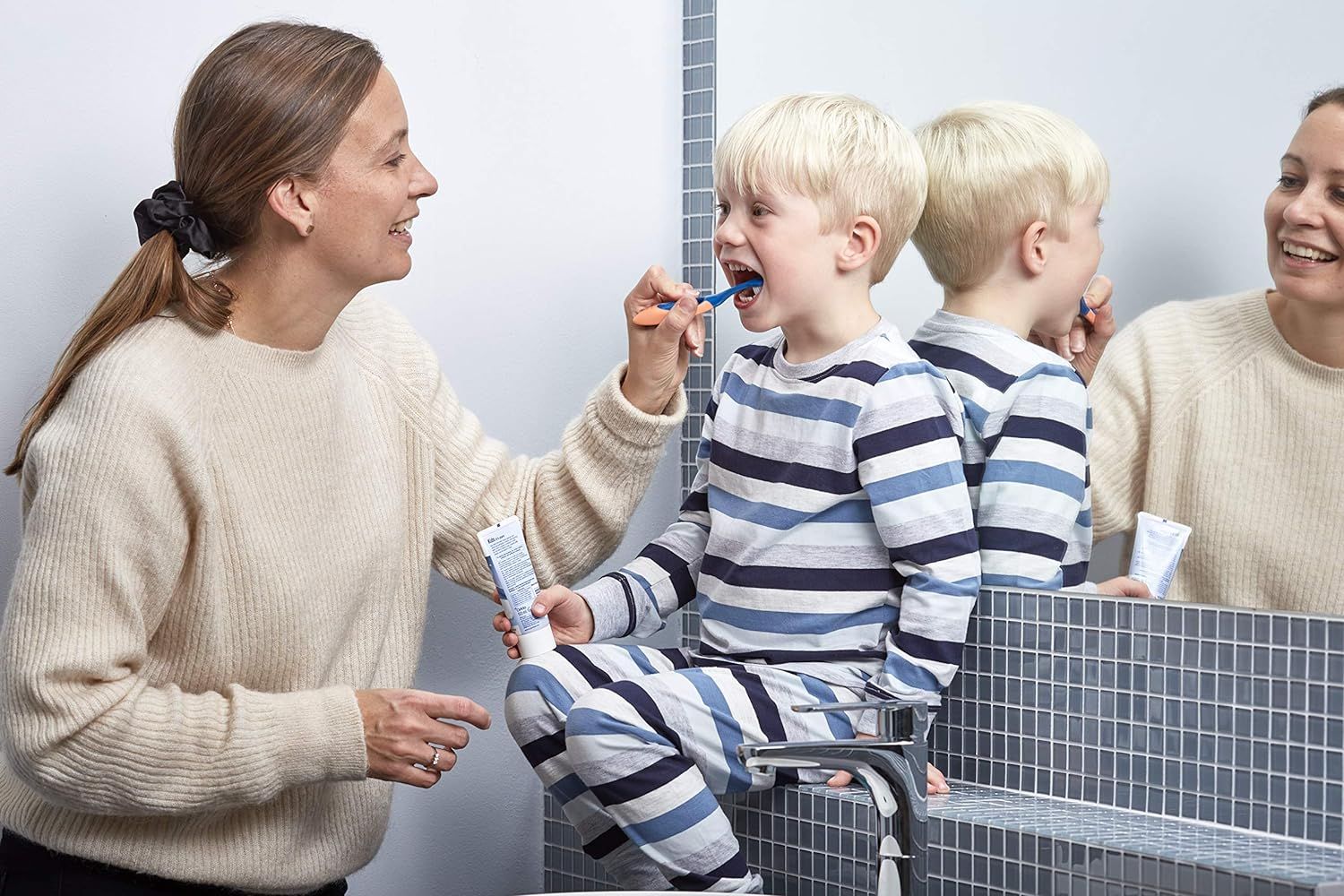 Une mère aide son enfant à se brosser les dents dans la salle de bain.