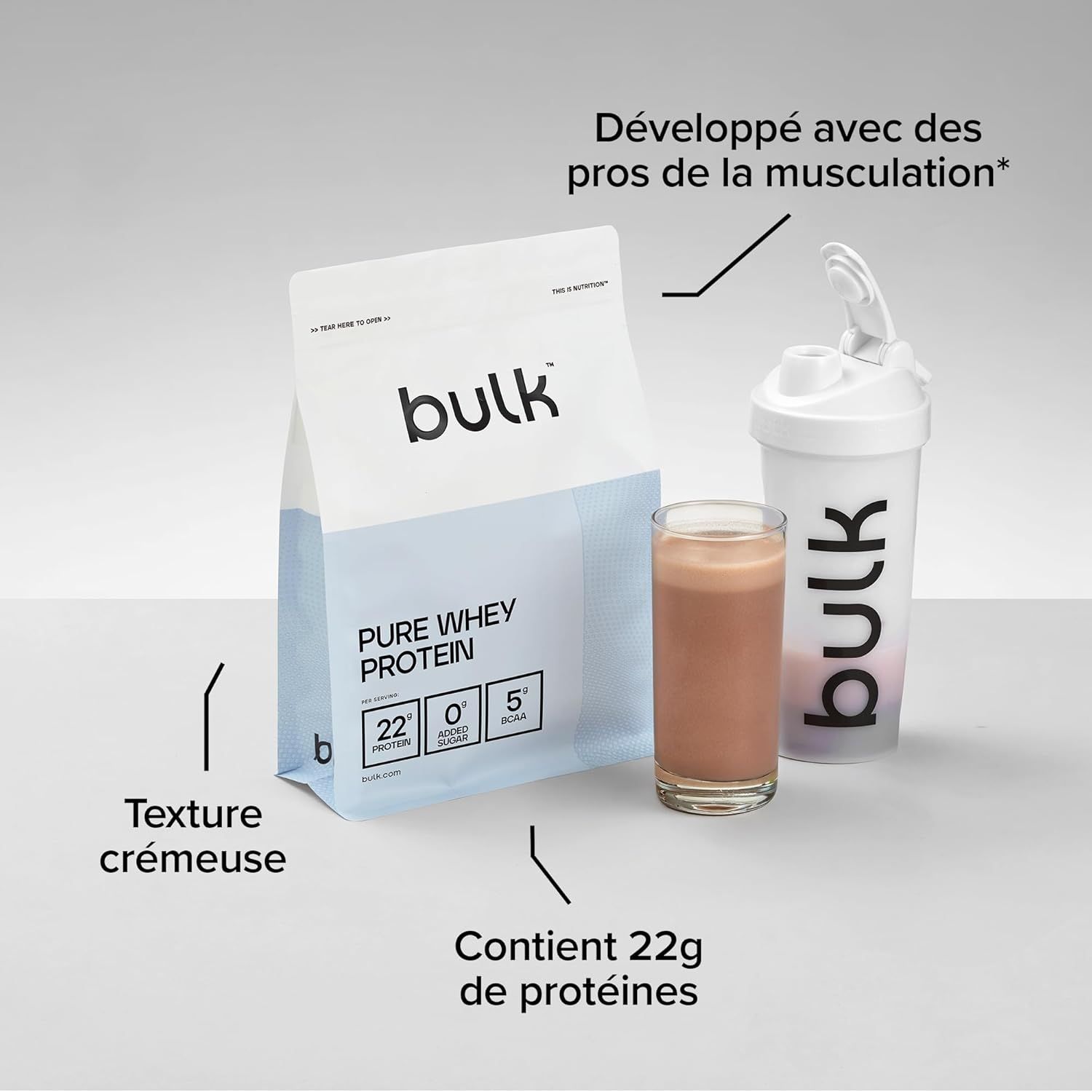 Un paquet de Bulk Pure Whey Protein à côté d'un verre de boisson chocolatée et d'un shaker blanc.
