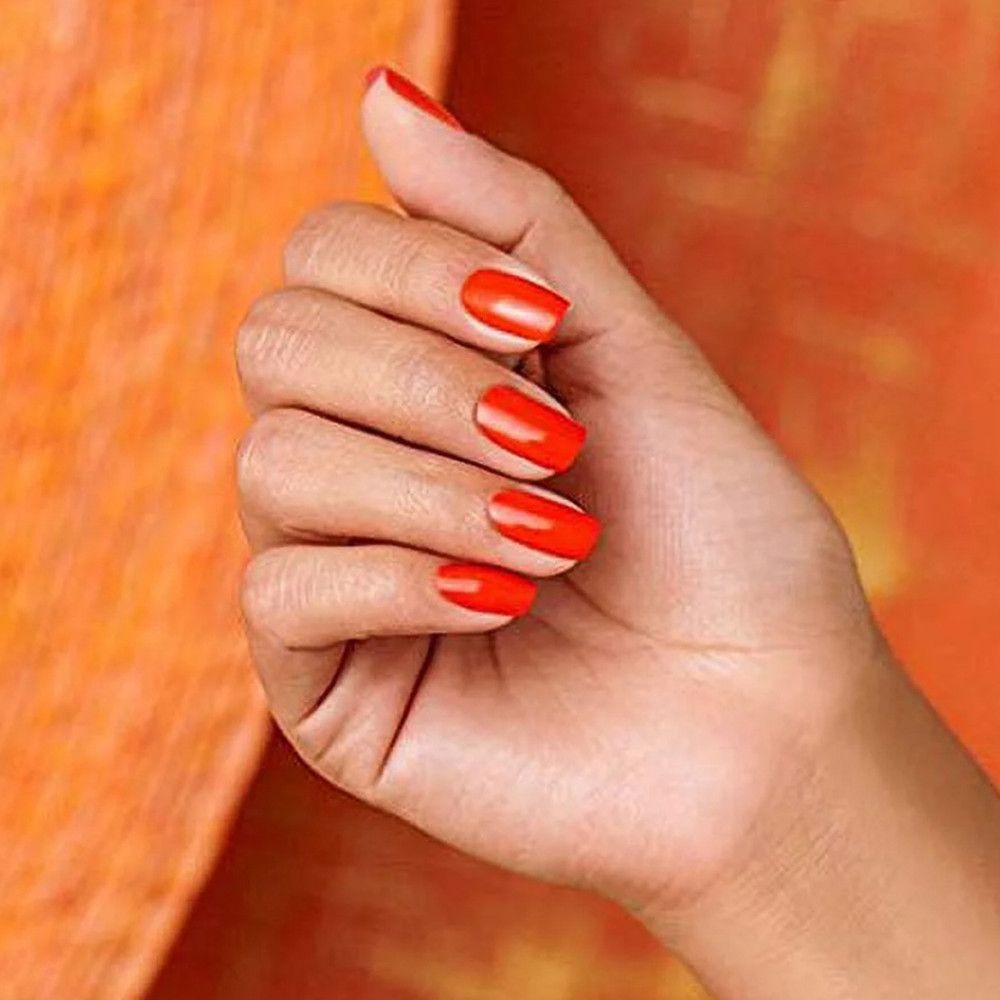 Main avec ongles vernis orange vif. Les ongles sont courts et de forme carrée.