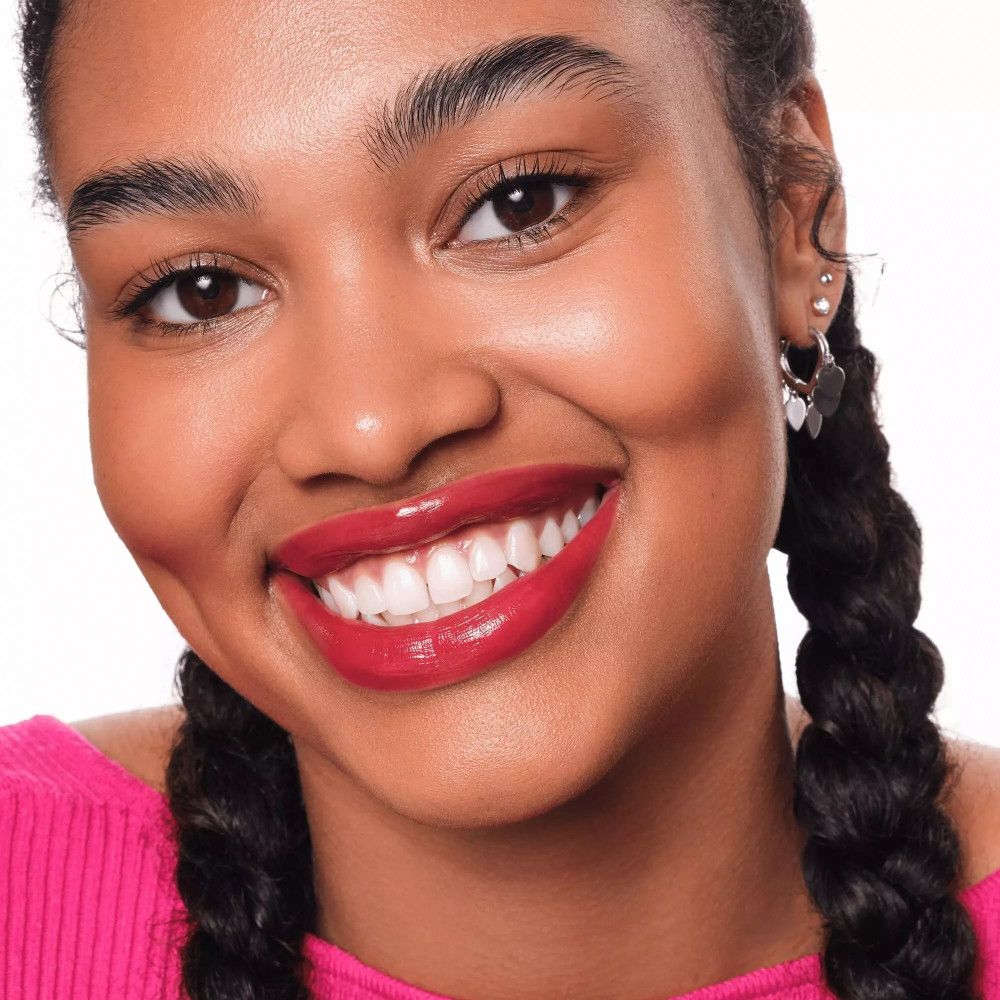 Portrait d'une femme souriante. Rouge à lèvres rouge. Tresses. Haut rose. Peau foncée.