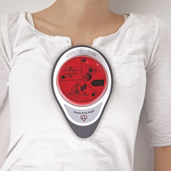 Cardio First Angel sur la poitrine. Bouton rouge avec instructions, cadre blanc, mousse grise. Texte: Cardio First Angel.