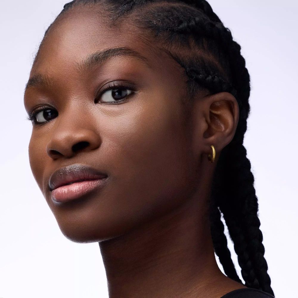 Portret van een persoon met een donkere huid. Ze heeft gevlochten haar en draagt gouden oorbellen.