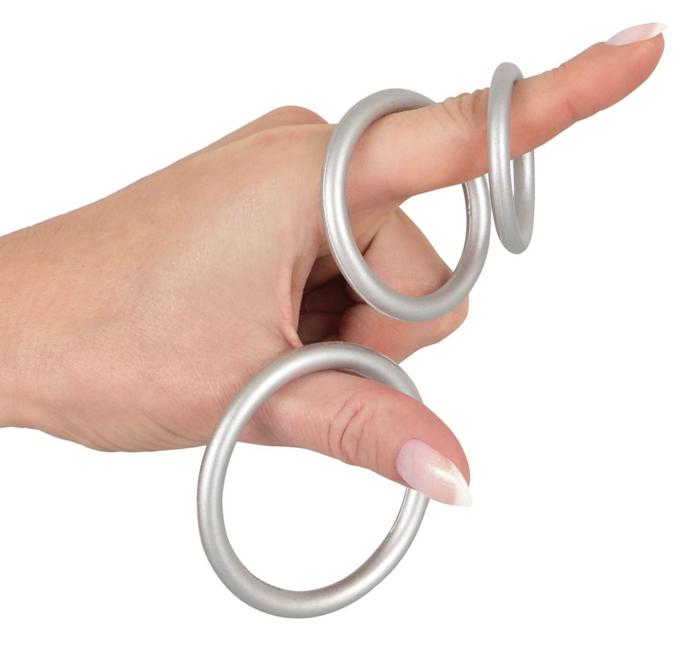 Main avec trois anneaux de pénis argentés métalliques en silicone flexible sur les doigts.