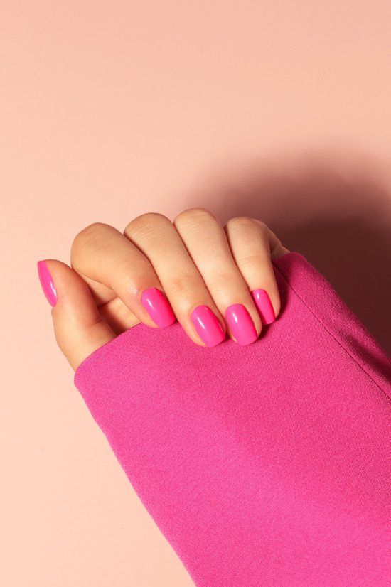 Main avec ongles vernis roses. Fond rose. Manches d'un haut rose.