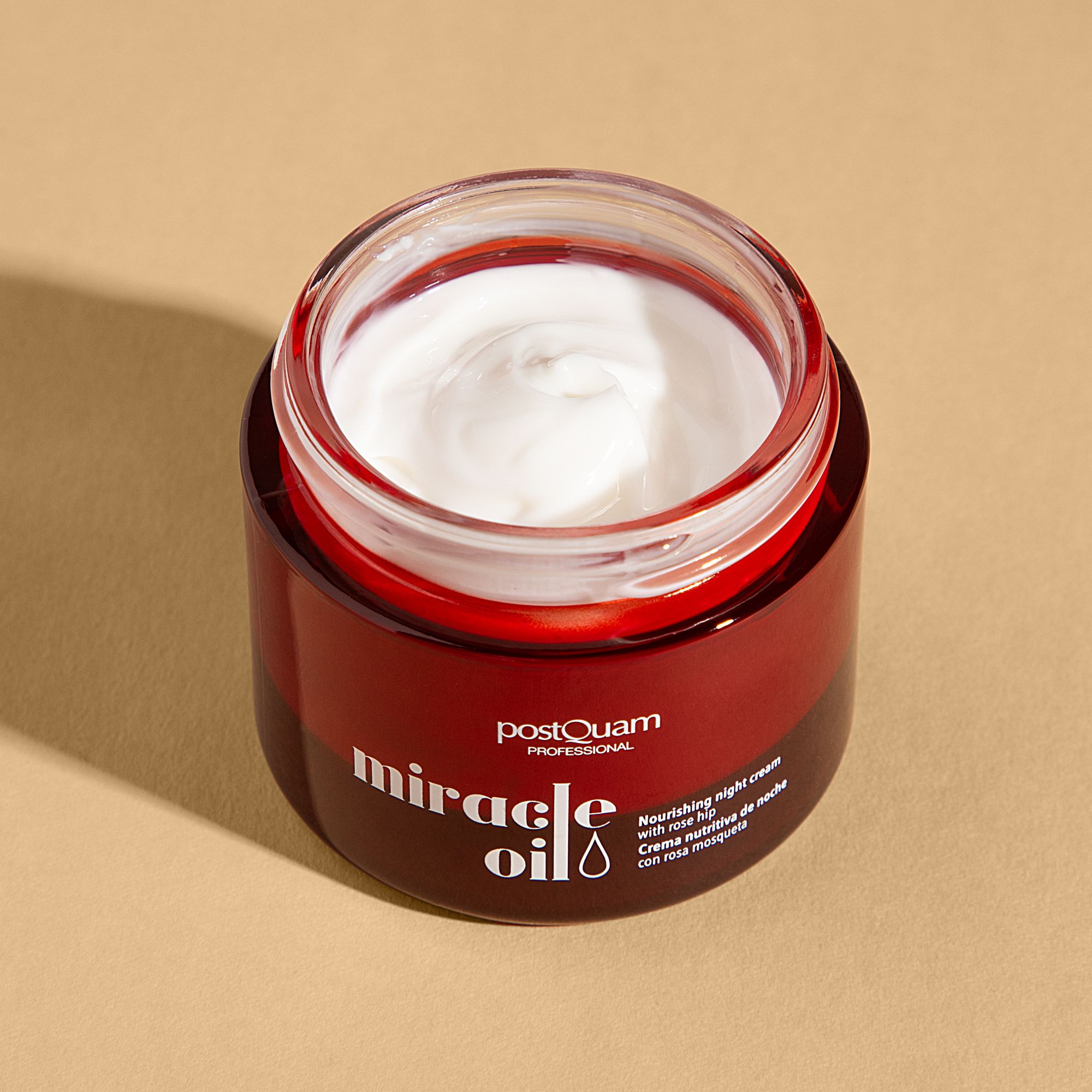 Pot rouge ouvert avec crème blanche. Inscription : "postQuam PROFESSIONAL miracle oil". Texte : "Nourishing night cream with rose hip".