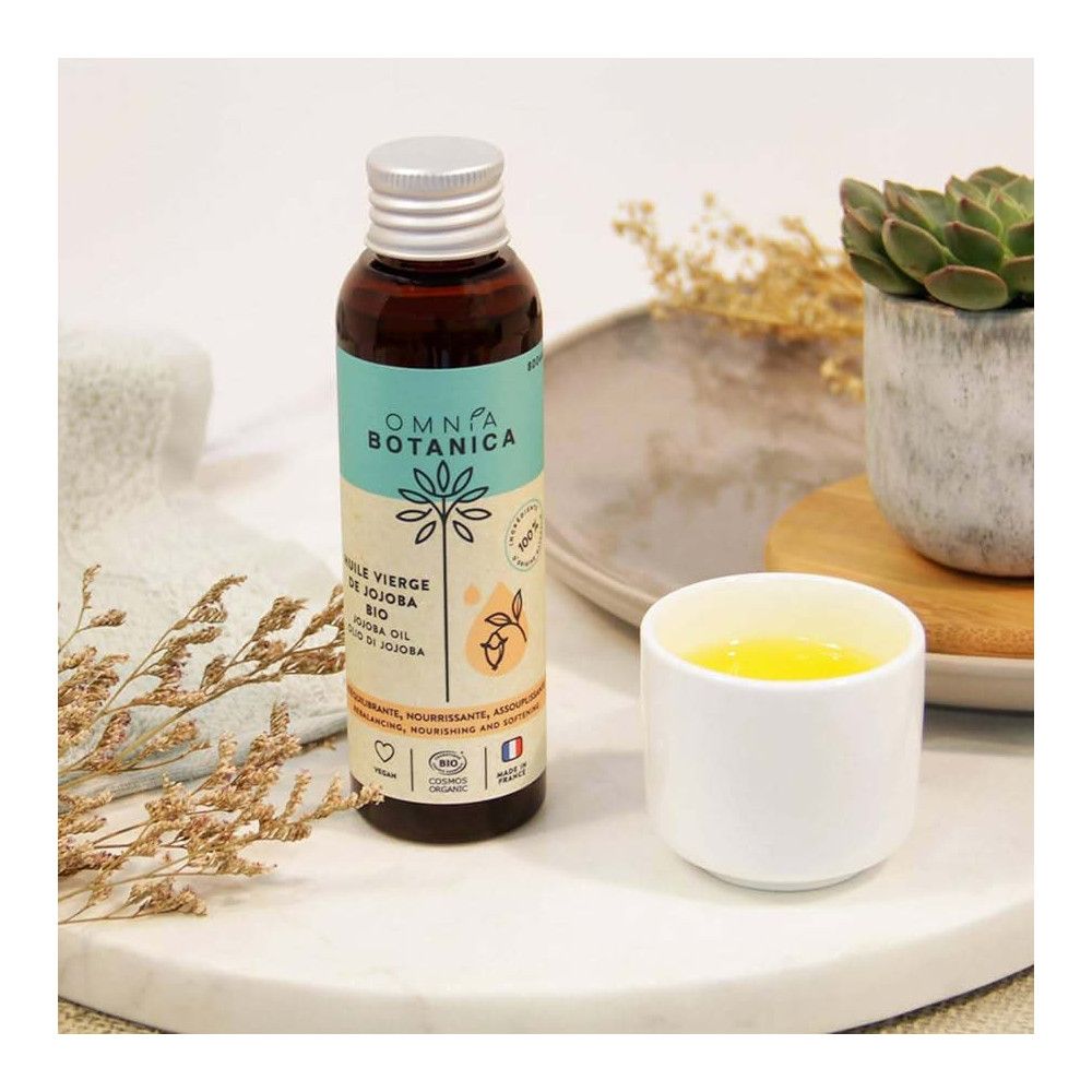 Bruine glazen fles met zilveren dop. Etiket met productnaam en logo. Naast een witte beker met gele vloeistof.