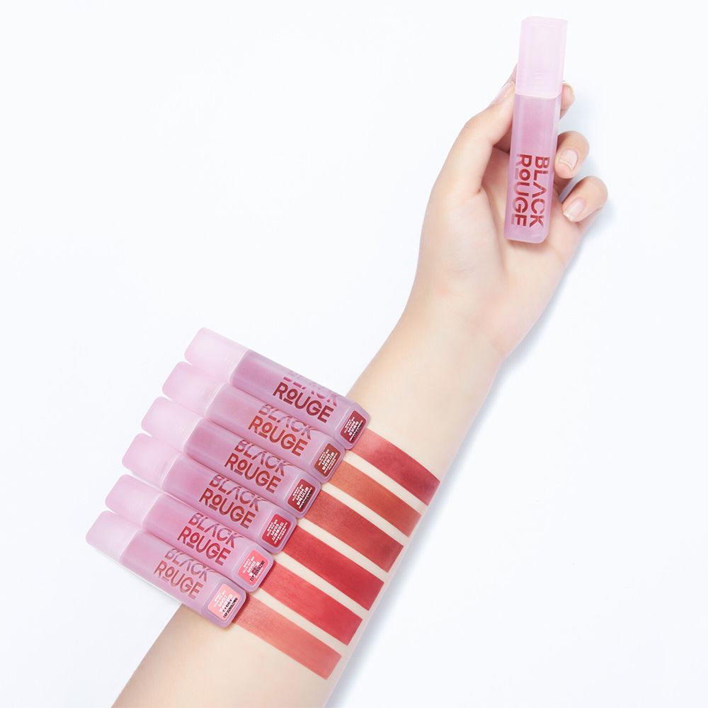 Main avec des tubes de gloss et des échantillons de couleurs sur le bras. BLACK ROUGE est écrit sur les tubes. Les couleurs sont brun-rouge.