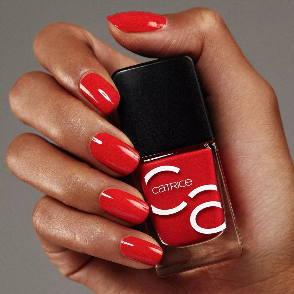 Main avec ongles rouges vernis et flacon de vernis à ongles. Catrice est écrit sur le flacon.