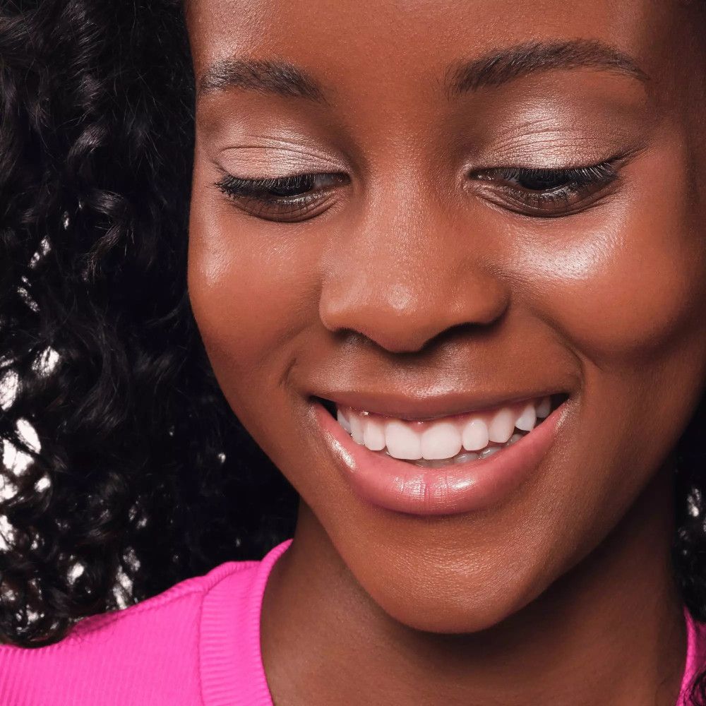 Gros plan d'une femme avec du fard à paupières crème sur les paupières. Elle sourit. Le fard est clair et scintillant.