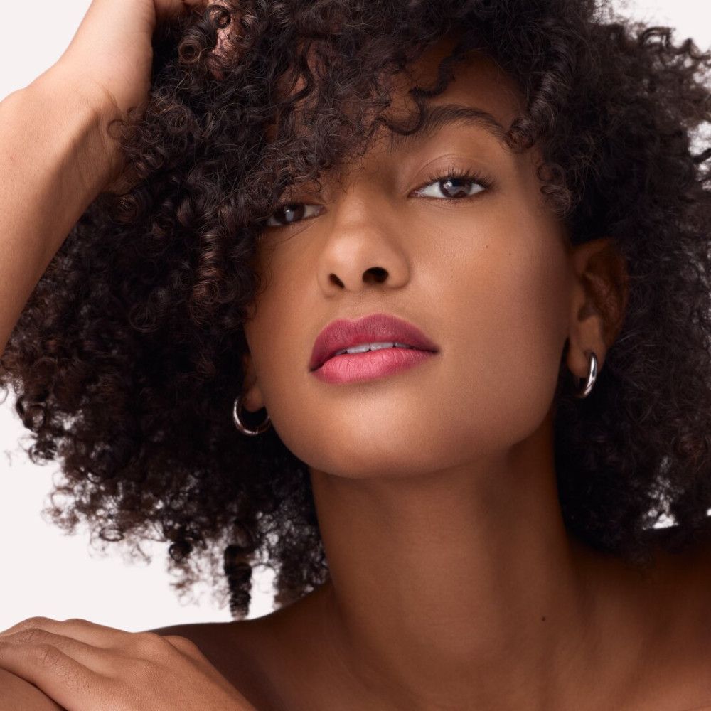 Portrait d'une femme avec des boucles et du rouge à lèvres rouge. Elle porte des boucles d'oreilles.
