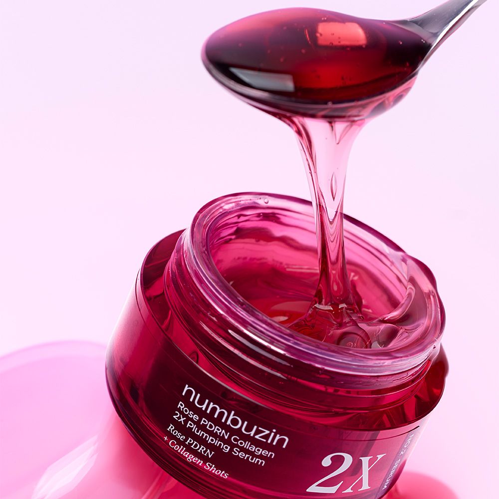 Een lepel NUMBUZIN Rose PDRN Collagen 2X Plumping Serum druppelt in een open rode pot.