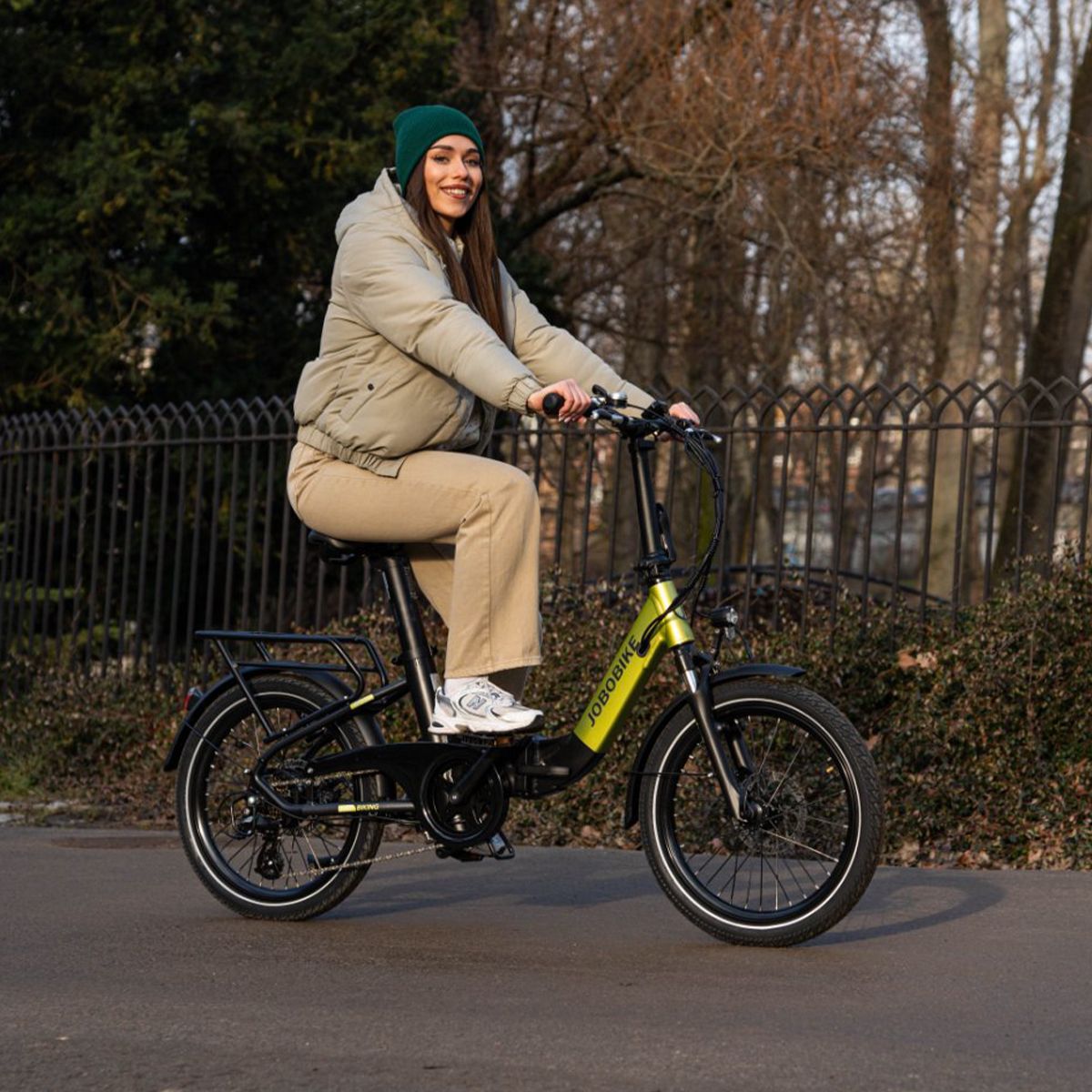 Vélo électrique pliable vert et noir. Logo JOBOBIKE. Porte-bagages, garde-boue. Personne sur un chemin.