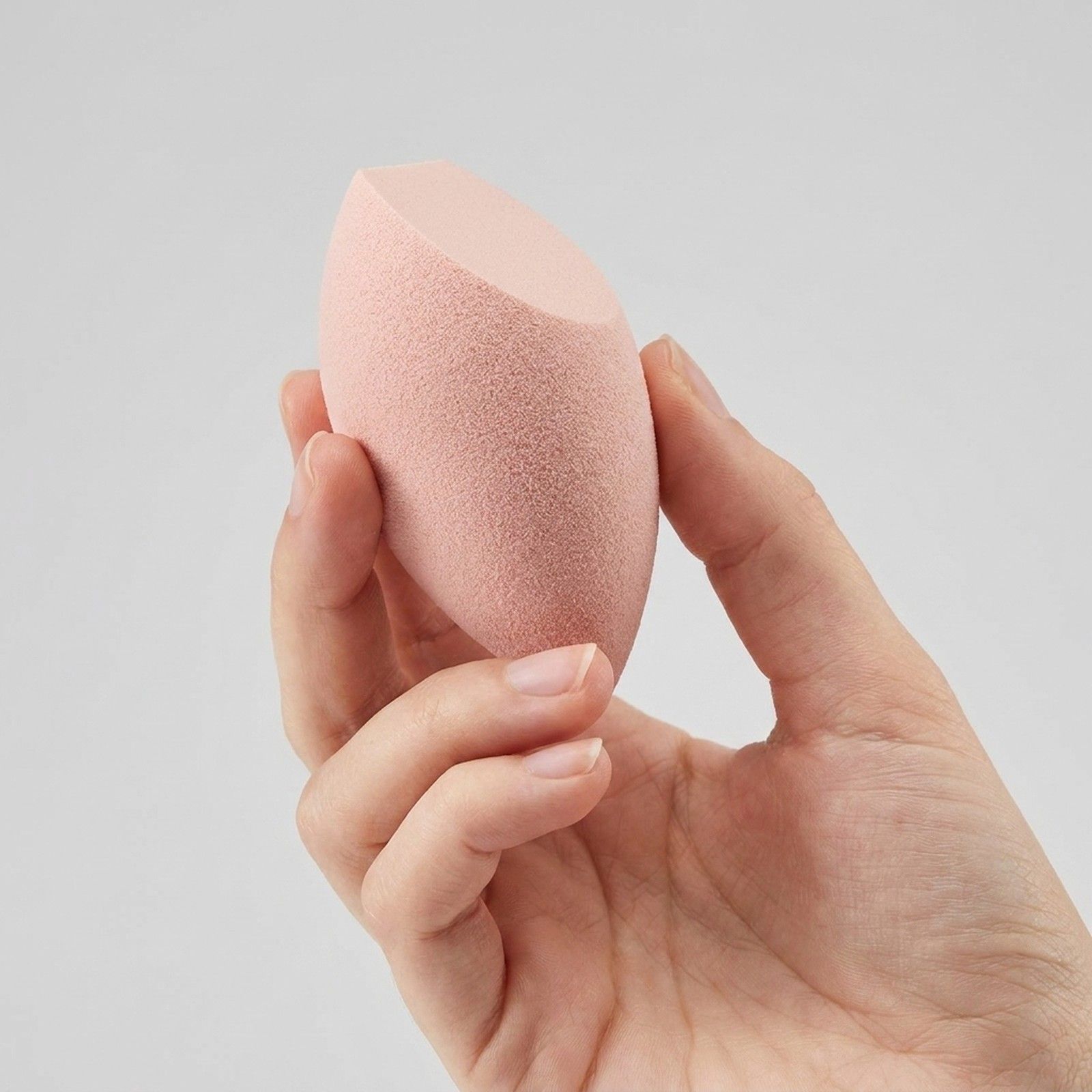 Een hand houdt een roze make-upspons met schuine punt vast.