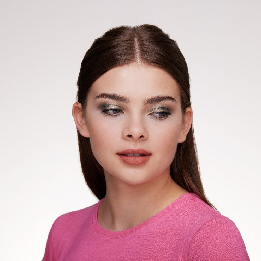 Portret van een vrouw met groene oogschaduw. Ze draagt een roze top.