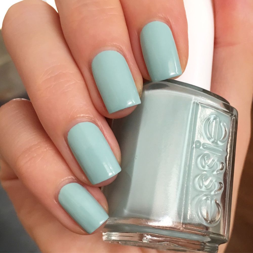 Hand met gelakte nagels en nagellakfles. Pastelblauwe nagellak. Fles met witte dop, merk Essie.