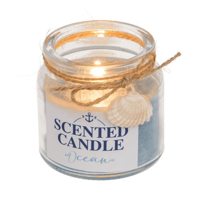 Bougie parfumée allumée en verre. Cire bleue, étiquette avec ancre et texte "SCENTED CANDLE Ocean". Décorée d'un coquillage et cordon.