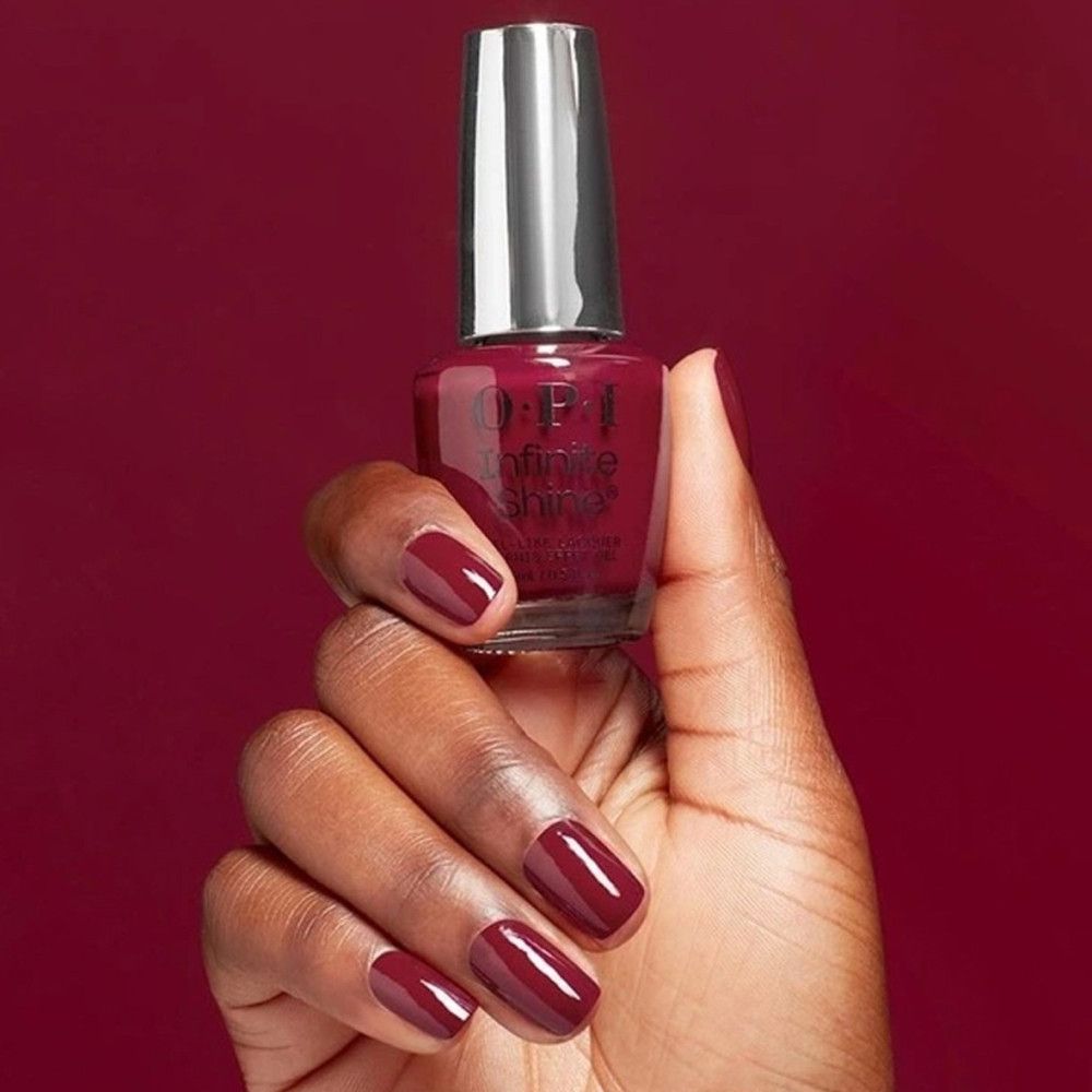 Flacon de vernis à ongles OPI Infinite Shine, bouchon argenté. Ongles et flacon de vernis rouge foncé.