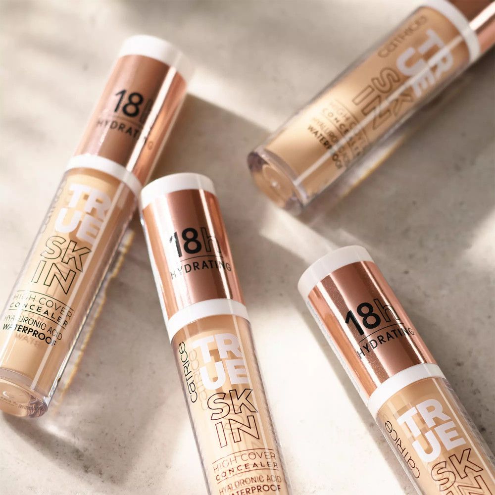 Plusieurs flacons de correcteur. Inscription: True Skin, High Cover Concealer, 18h Hydrating, Acide Hyaluronique, Waterproof.
