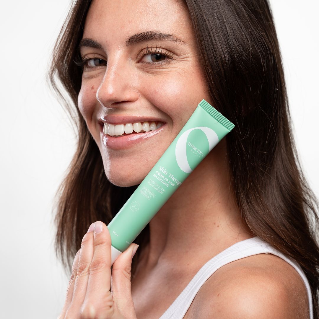 Femme tenant un tube vert. Le tube porte l'inscription "Skin Therapy". Elle sourit.