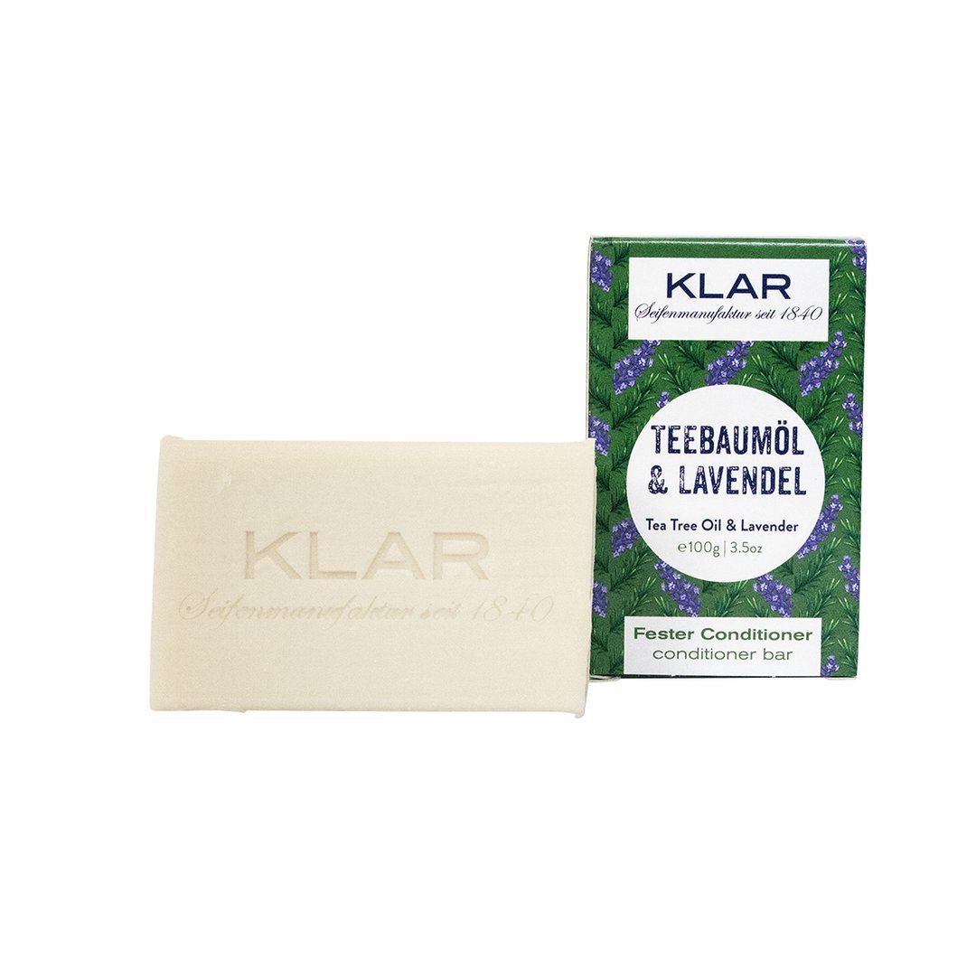 Savon rectangulaire à côté d'un emballage vert. Savon avec logo KLAR. Emballage : Teebaumöl & Lavendel, Fester Conditioner.