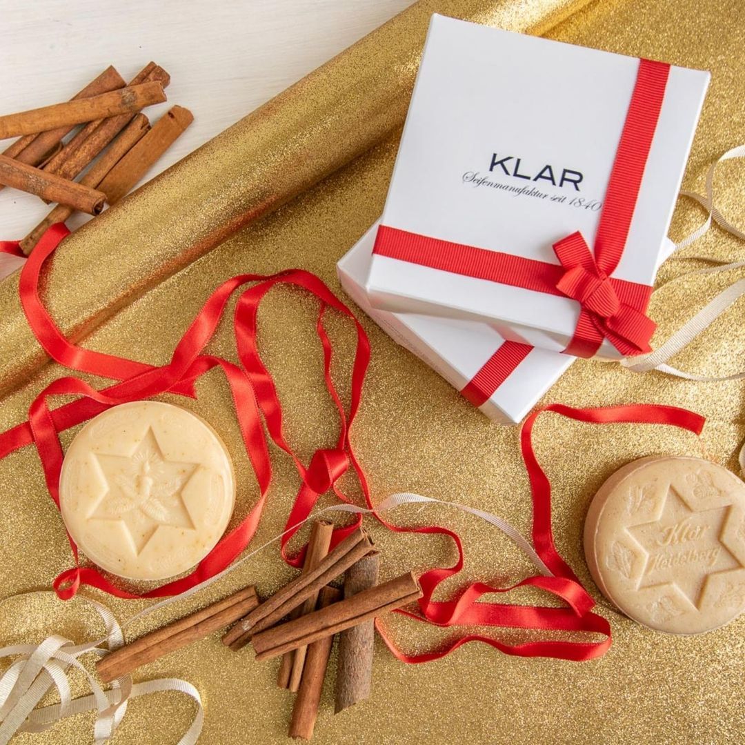 Twee ronde zepen met sterpatroon. Witte geschenkdoos met rode lint. Kaneelstokjes en gouden achtergrond.