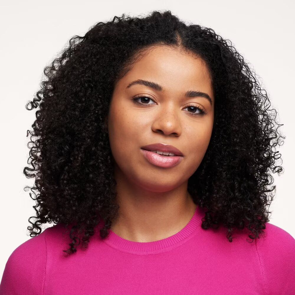 Portrait d'une femme aux cheveux bouclés et aux lèvres roses. Elle porte un haut rose.